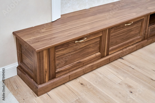 Elegant new TV cabinet made of veneer and solid walnut lumber with gold handles near wall in light room close upper view