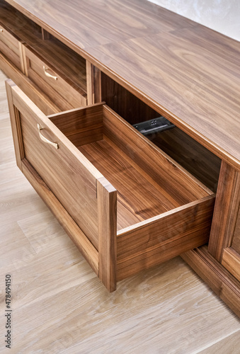 Elegant new TV cabinet made of veneer and solid walnut lumber with gold handles near wall in light room close upper view