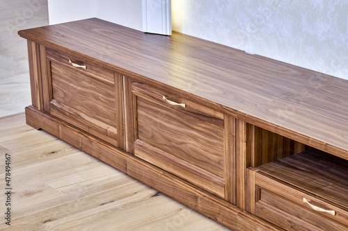 Elegant new TV cabinet made of veneer and solid walnut lumber with gold handles near wall in light room close upper view