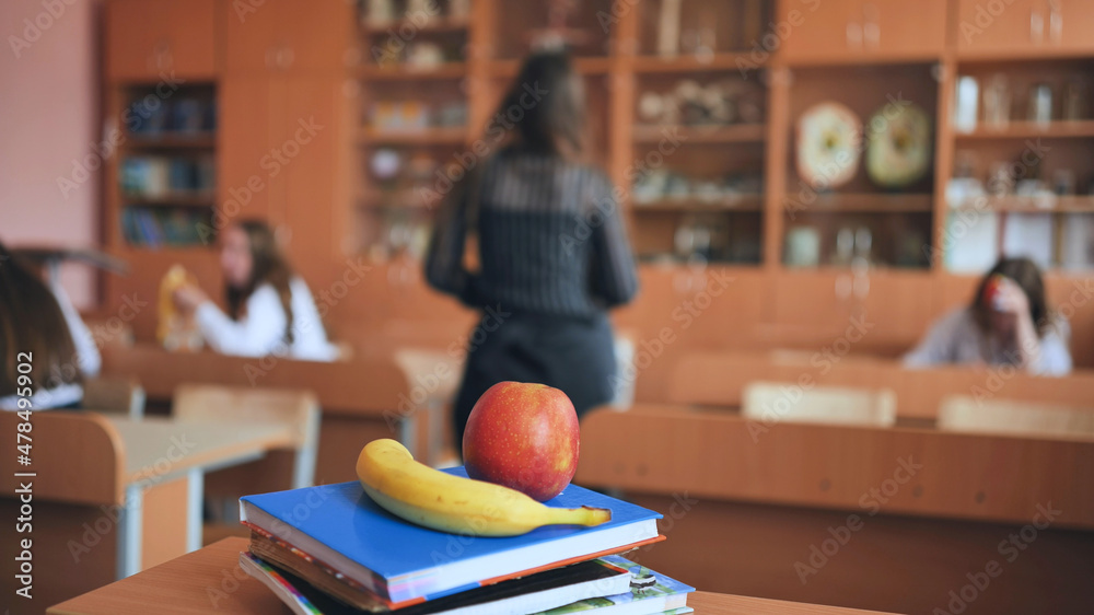 An apple and a banana lie on the books in an empty classroom between lessons. An apple and a banana lie on the books in an empty classroom between lessons.