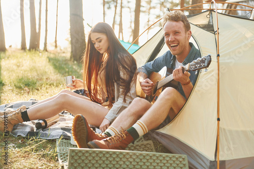 Guy playing guitar. Young couple is traveling in the forest at daytime together