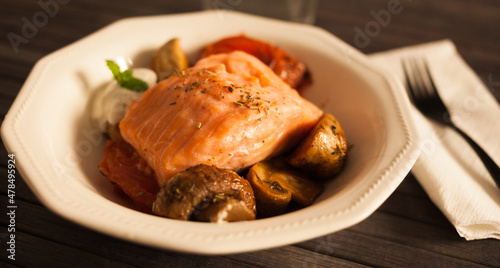 steamed sea trout fillet served on fried mushrooms with tomatoes in a white bowl