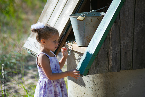 Surprised pretty little girl in country style staying near to well. High quality photo