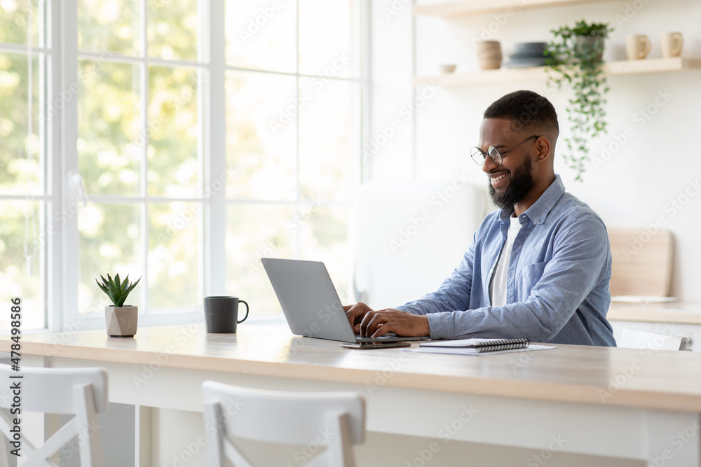 Glad millennial african american man with beard in glasses chatting remotely, work on computer alone Glad millennial african american man with beard in glasses chatting remotely, work on computer alone