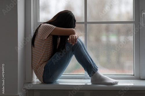 Foto Upset long-haired brunette girl sitting on windowsill and crying