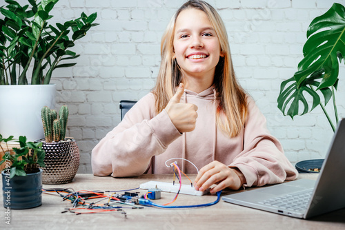 A teenager girl with her thumb up studying robotics at home, stem and arduino coding classes for children photo
