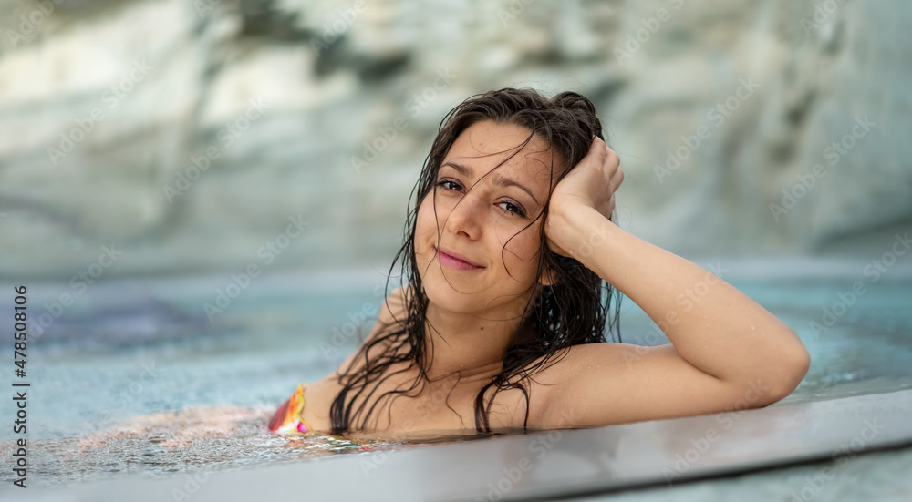 Panorama portrait of beautiful young natural sexy woman with dark hair  relaxes contend happy in colorful flower bikini in holidays summer sun in  the blue spa wellness hot tub pool Stock Photo