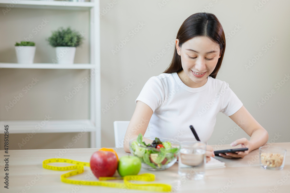 asian females using smartphones and taking notes eating healthy food each day with vegetables fruit on table. health and care concept.