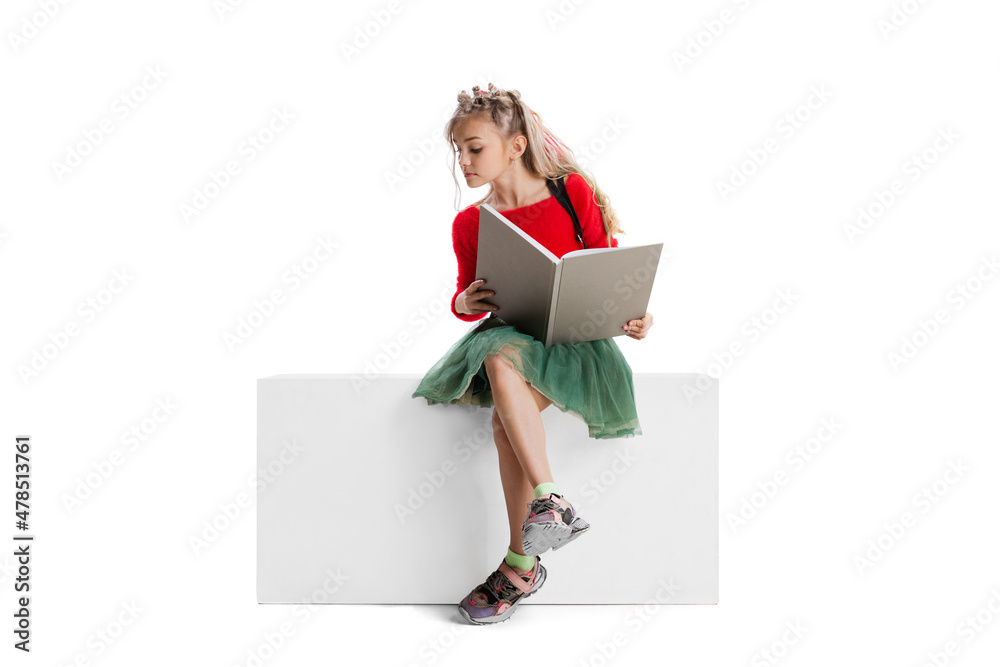 One beautiful little cute girl in casual clothes sitting on big box isolated on white studio background. Happy childhood concept. One beautiful little cute girl in casual clothes sitting on big box isolated on white studio background. Happy childhood concept.