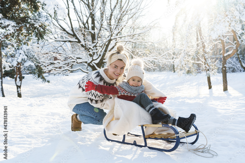 Young mother and her cute little son with retro sled in a snowy park during sunny day Young mother and her cute little son with retro sled in a snowy park during sunny day