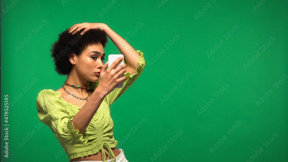 young african american woman in blouse looking at smartphone isolated on green young african american woman in blouse looking at smartphone isolated on green