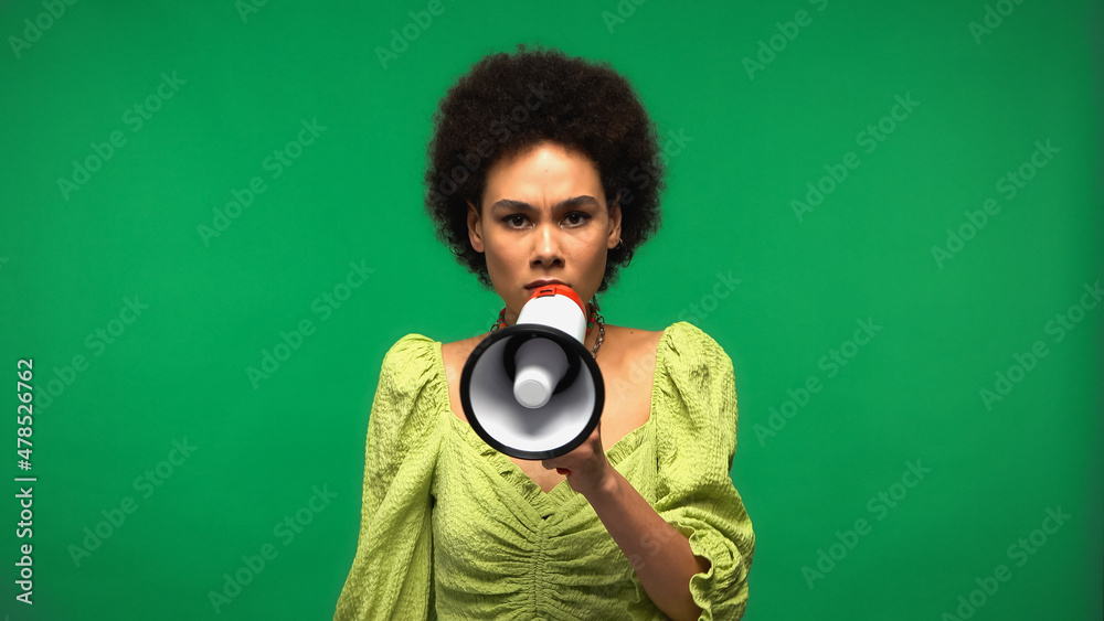 Obraz premium african american woman holding megaphone and looking at camera isolated on green
