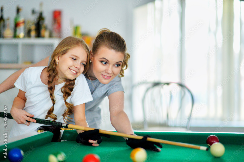 Fototapeta premium Portrait of little cute girl with mother playing billiards