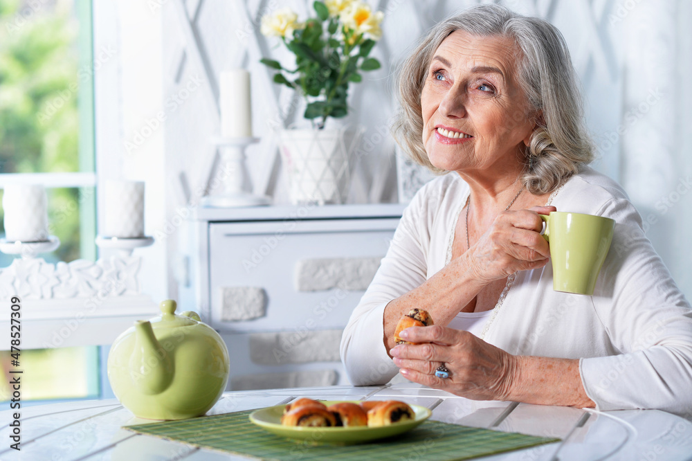 Portrait of beautiful smiling senior woman drinking tea while sitting at kitchen table