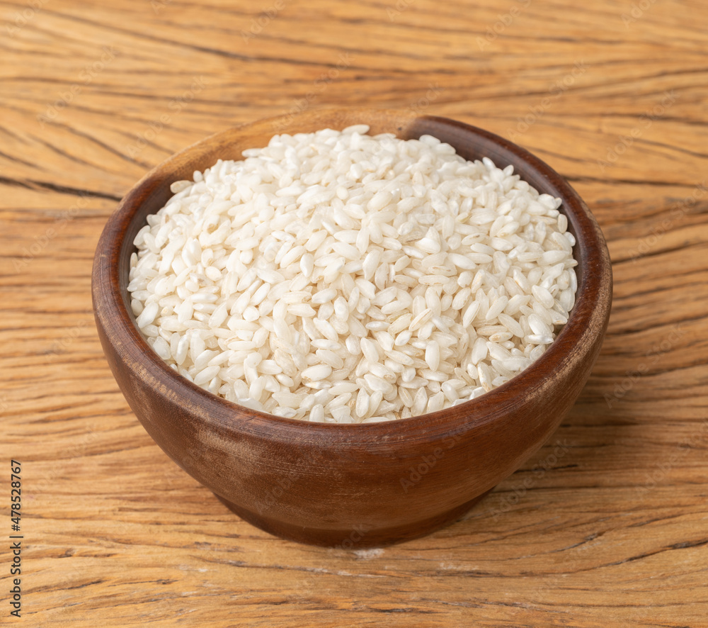 Raw carnaroli risotto rice in a bowl over wooden table Raw carnaroli risotto rice in a bowl over wooden table
