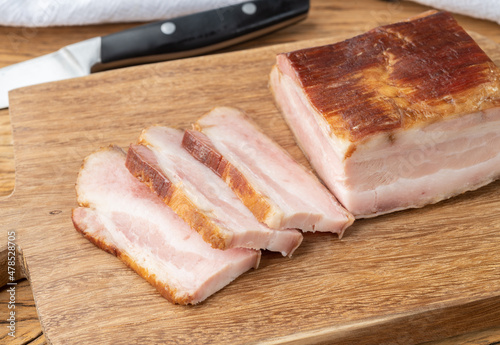 Smoked bacon with slices and knife over wooden board
