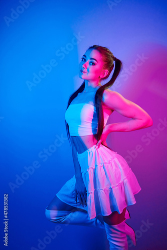 In skirt. Fashionable young woman standing in the studio with neon light