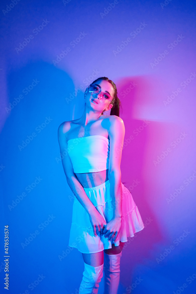 White clothes. Fashionable young woman standing in the studio with neon light