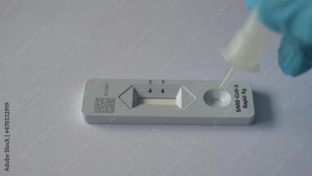 The doctor is dropping a solution containing a sample from the patient's nasal cavity onto the Antigen test kit for COVID-19 testing on a white background. The doctor is dropping a solution containing a sample from the patient's nasal cavity onto the Antigen test kit for COVID-19 testing on a white background.