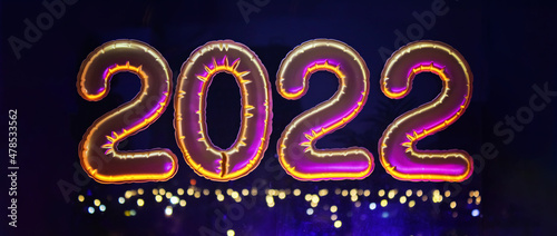 Gold inflatable foil balloons numbers 2022 on the window against the background of the night city, in neon light. New year 2022, christmas. Banner