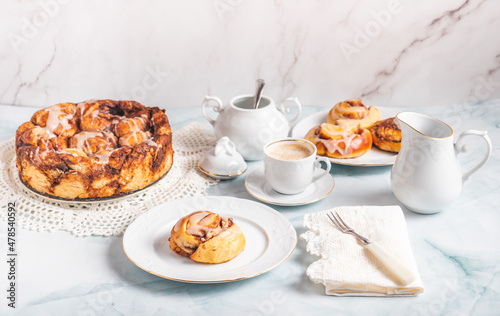 Homemade cinnamon rolls on a white plate on a white table with coffee and pastry buns for breakfast. Traditional Swedish and Danish recipe.