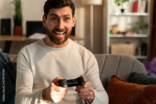 Excited young man playing video games and making winner gesture, while sitting at the sofa