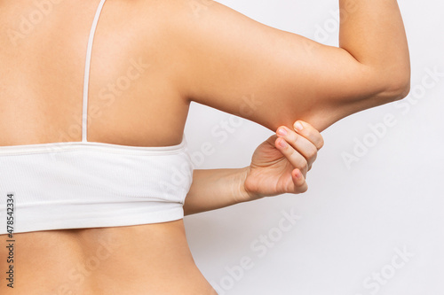 Cropped shot of a young woman grabbing skin on her upper arm with excess fat isolated on a white background. The loose and saggy muscles of a back and arms. Overweight. Excess weight on the upper body