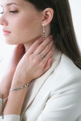 Trending silver jewelry set on a beautiful young girl in a white fashionable jacket with long dark hair. Beauty and fashion 