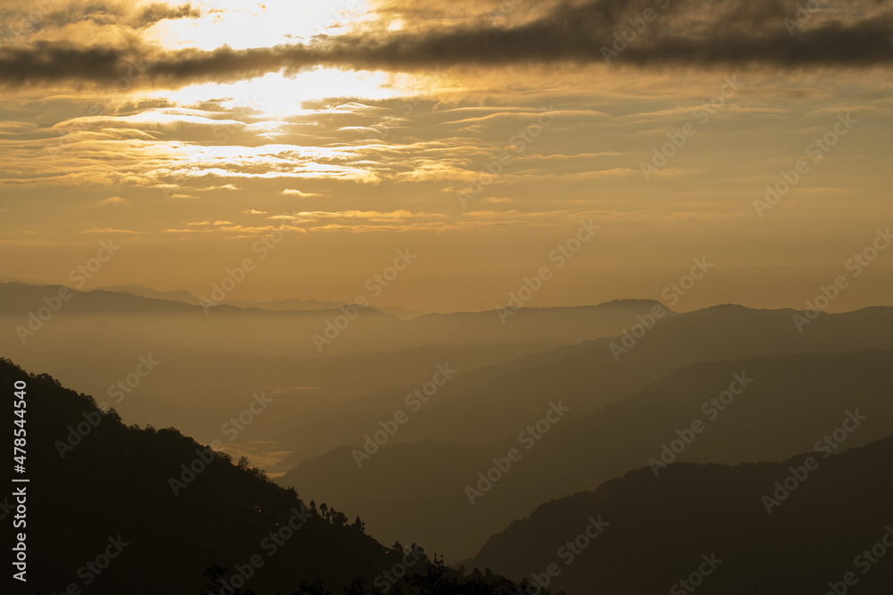 Sunrise scene as seen from Okhrey, Sikkim, India. Sun rising from the back of mountain with orange glow. Fog in the middleground of the picture.
