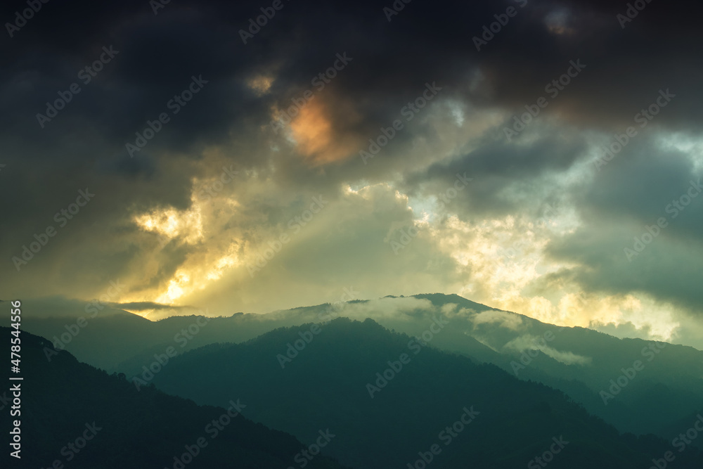 Light coming through window of clouds from setting sun, over Himalayan Mountain peaks. Dramatic cloud formation with sunset colours over Indian Mountain peaks.