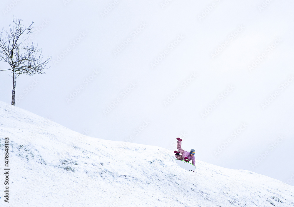 A child very quickly slides down a snow-covered mountain on a sled. Winter walk