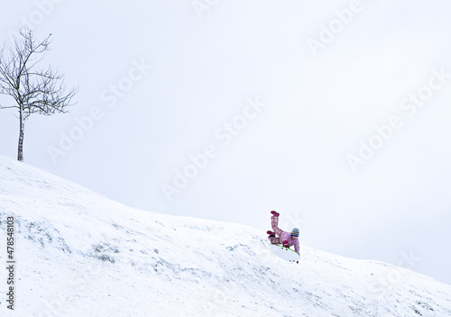 A child very quickly slides down a snow-covered mountain on a sled. Winter walk