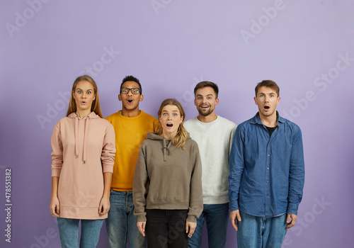 Portrait of cheerful funny five surprised and amazed young people on light purple background. Multiracial women and men in casual clothes with wide open eyes and mouths look at camera. Banner.