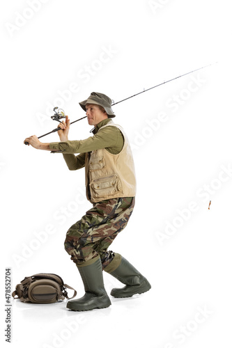 Portrait of young man, professional fishman with fishing rod, spinning and equipment going to river isolated over white studio background