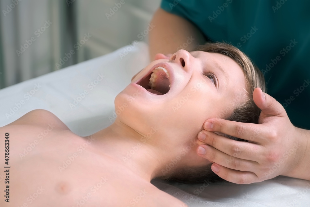 Session of craniosacral therapy, cure of teen boy's jaw by a doctor therapist. Craniosacral therapist touches the boy's cheeks and checks the correctness of the jaws at the hospital.