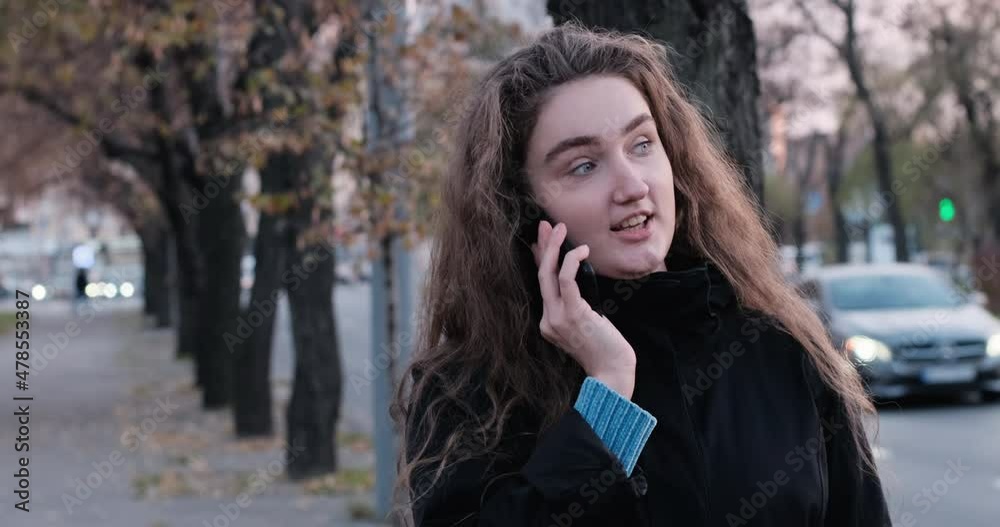 Cheerful pretty schoolgirl talking on phone and look straight ahead. Girl with abundant brown hair talking on the mobile phone. Cheerful pretty schoolgirl talking on phone and look straight ahead. Girl with abundant brown hair talking on the mobile phone.