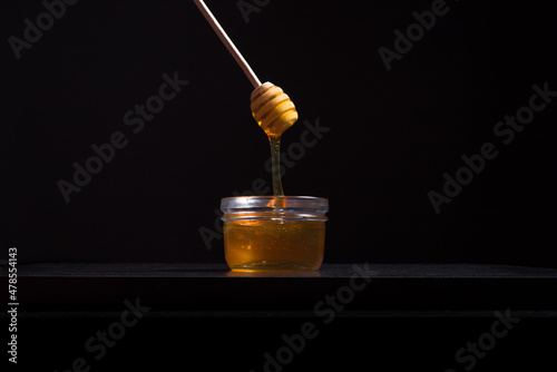 Verter miel de abeja con un gotero de madera en un frasco de vidrio sobre fondo negro. Aislado