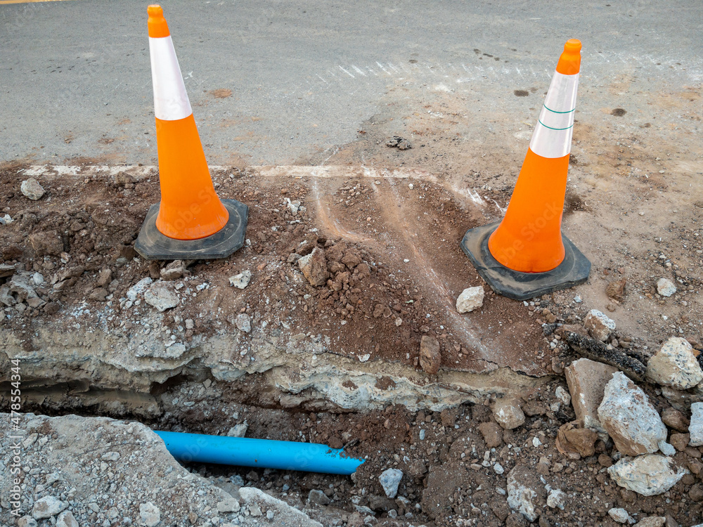The new PVC pipe is laying in the trench near the asphalt road for the