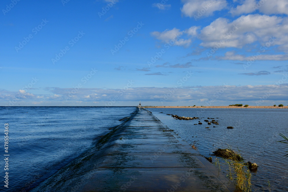 A view of a vast walkway leading right into the sea with water reservoirs on both sides and some small beach visible in the distance spotted on a sunny summer day on a Polish countryside