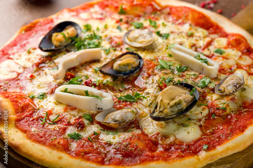 Pizza with seafood, cheese and tomato sauce on wooden board macro close up