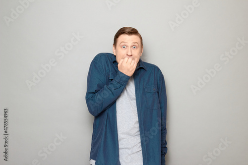 Portrait of shocked frightened blond mature man biting his nails