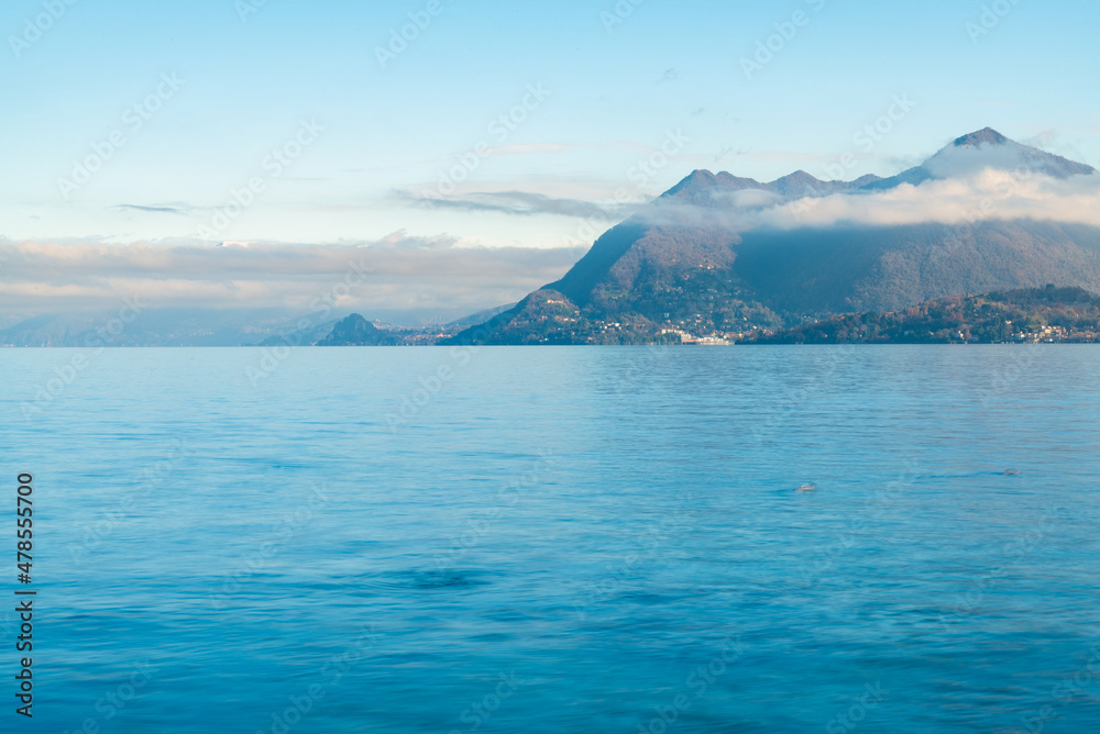 The calm waters of Lake Maggiore, Italy. Italian alps mountains with white clouds on the background. The calm waters of Lake Maggiore, Italy. Italian alps mountains with white clouds on the background.
