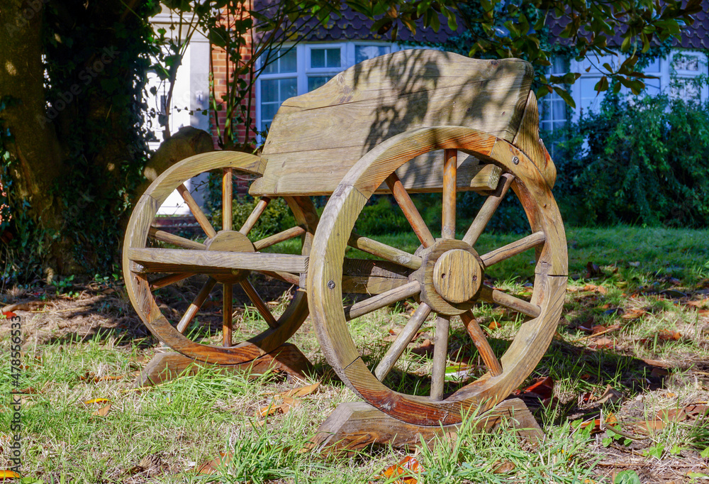 old wooden wagon made into a quirky garden seat. Crafted outdoor bench made from an old cart with wooden spoked wheels. 