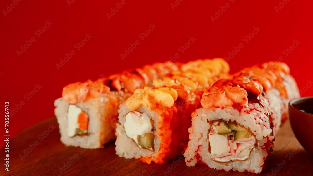 Sushi rolls near soy sauce. Set of tasty sushi rolls with cheese topped with sauce served on wooden table against red background in light room