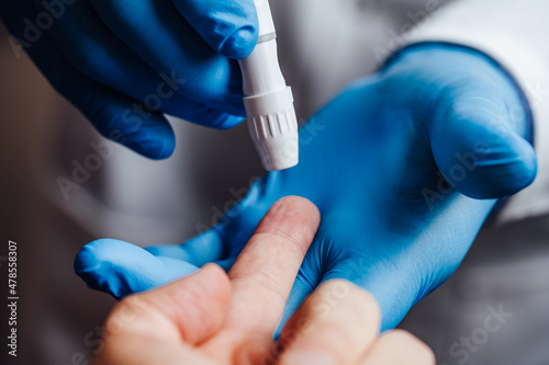 Doctor about to pierce a patient's finger with a lancet photo