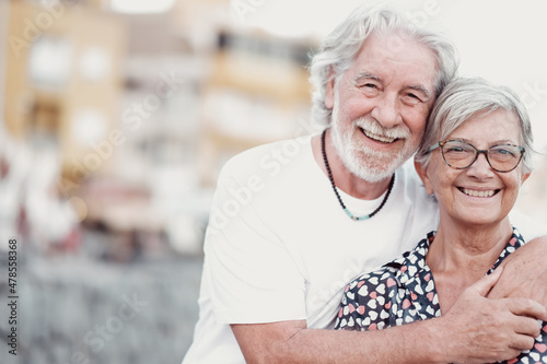 Happy couple of grandparents hug in outdoors smiling carefree. Beautiful caucasian people white haired