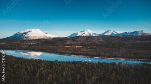 View of the wooded area and the Malselva River with a reflection on the snow-covered hills. Finnmark region, Nordland in northern Norway in beautiful sunny weather