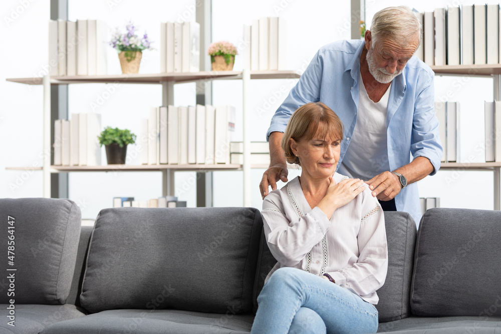 senior man giving a shoulder massage to his wife on sofa