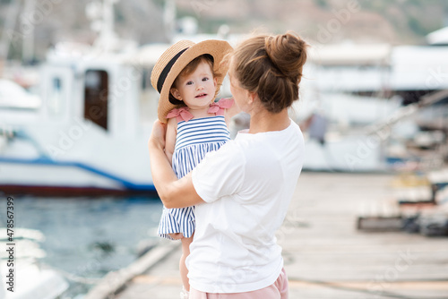 Mother with baby girl 1-2 year old with straw hat over sea and boats at background close up. Family lifestyle. Summer season. Childhood. © morrowlight