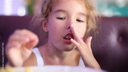 A 5-year-old girl is funny eating French fries in a cafe with her hands, chewing and making faces photo